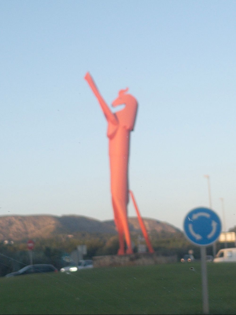 a blurry photo of a large orange cubist style sculpture of a horse on it's hind legs, in the middle of a traffic roundabout