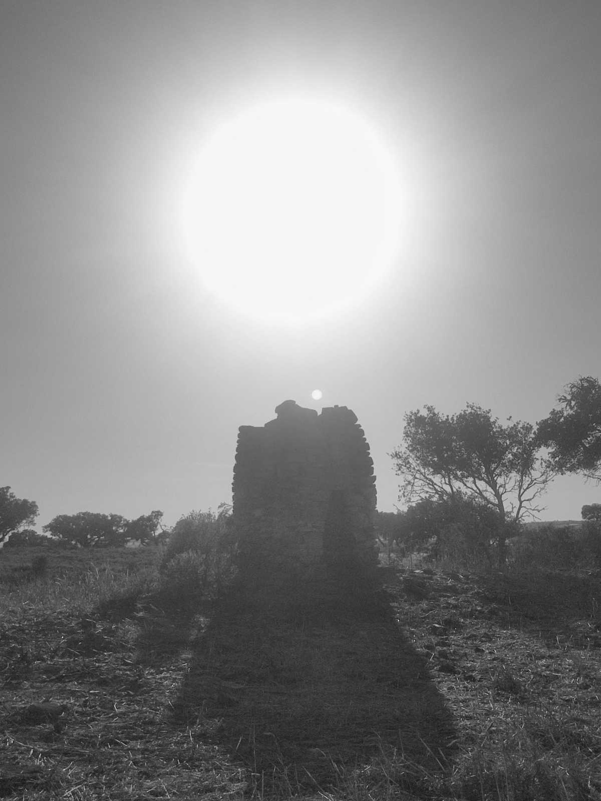 a stone shelter, all but silhouetted by the bright large sun, on a dry hill in the Alentejo