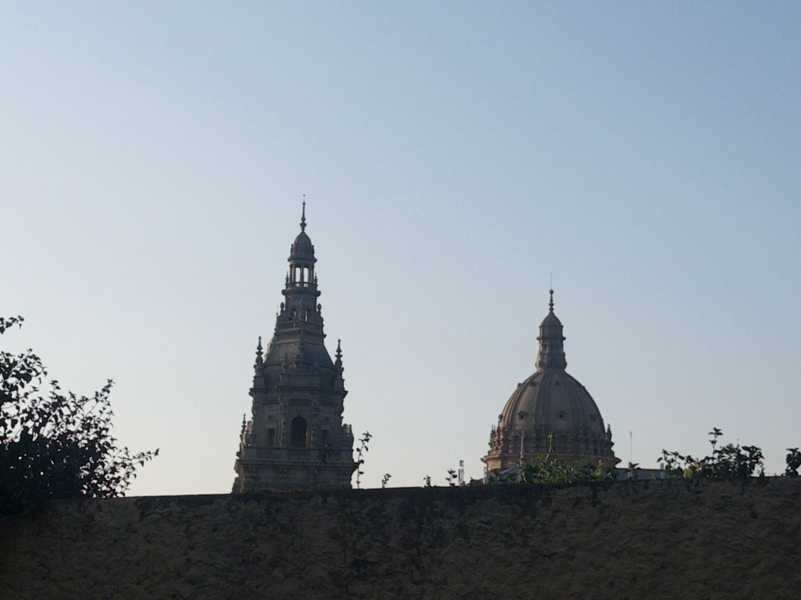 the spire and a dome of a great church emerge from behind a wall, alongside some bushes