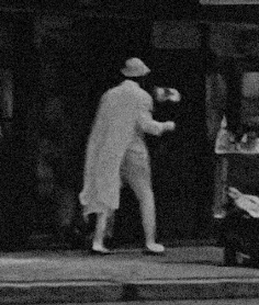 small black and white image of a man in a white cape and suit, holding what might be white flowers