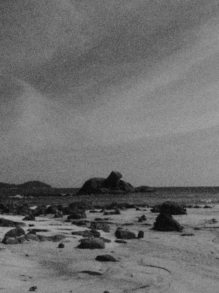 blurry black and white image of rocks on a beach and in the water