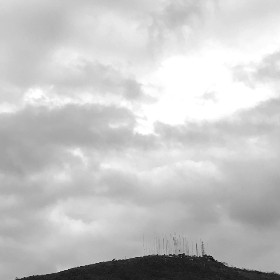 Grey photo of a hill, some clouds. There are a lot of aerials on the hill